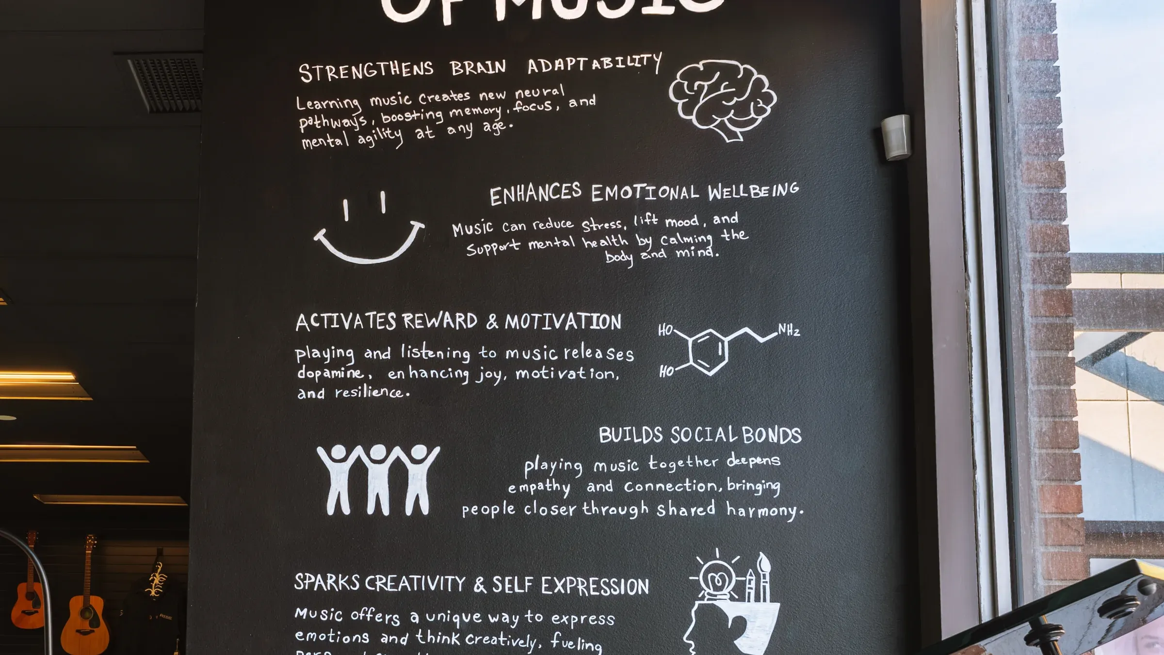 The Power of Music wall at Resonate Music School & Studio in Edmonton — five hand-painted categories on a black wall: Strengthens Brain Adaptability, Enhances Emotional Wellbeing, Activates Reward & Motivation, Builds Social Bonds, Sparks Creativity & Self Expression
